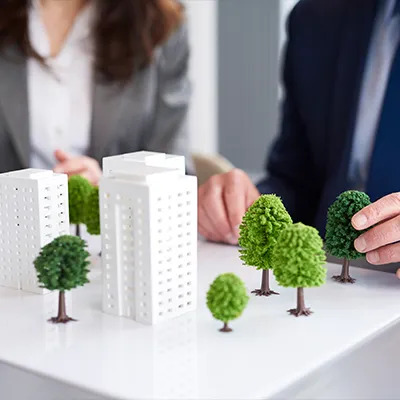 Immagine copertina corso online. Due persone sistemano un plastico di un'area verde con palazzi e alberi