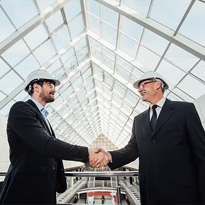 Immagine copertina corso online. Due uomini vestiti in giacca e cravatta e caschetto sicurezza sorridono e si stringono la mano